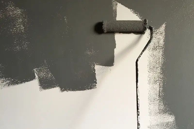 Corró amb pintura grisa sobre una paret parcialment pintada.